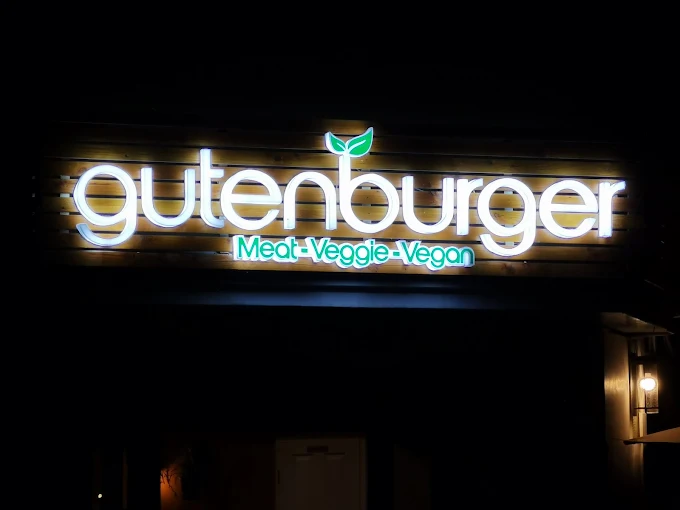 Beleuchteter Gutenburger Schriftzug auf einer Holzlamellen-Blende bei Nacht