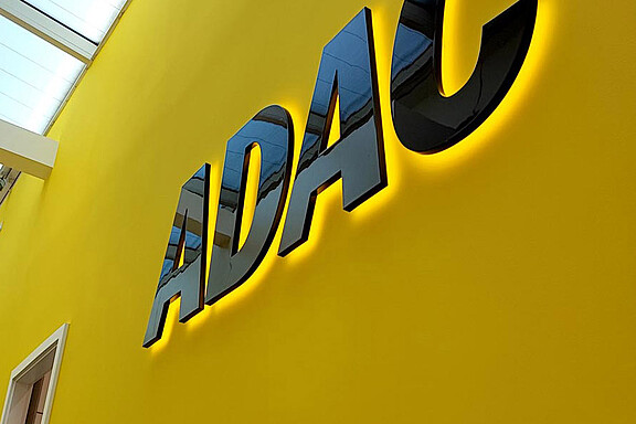 Schwarze dreidimensionale ADAC-Buchstaben mit warmer indirekter Hinterleuchtung auf einer gelben Innenwand.