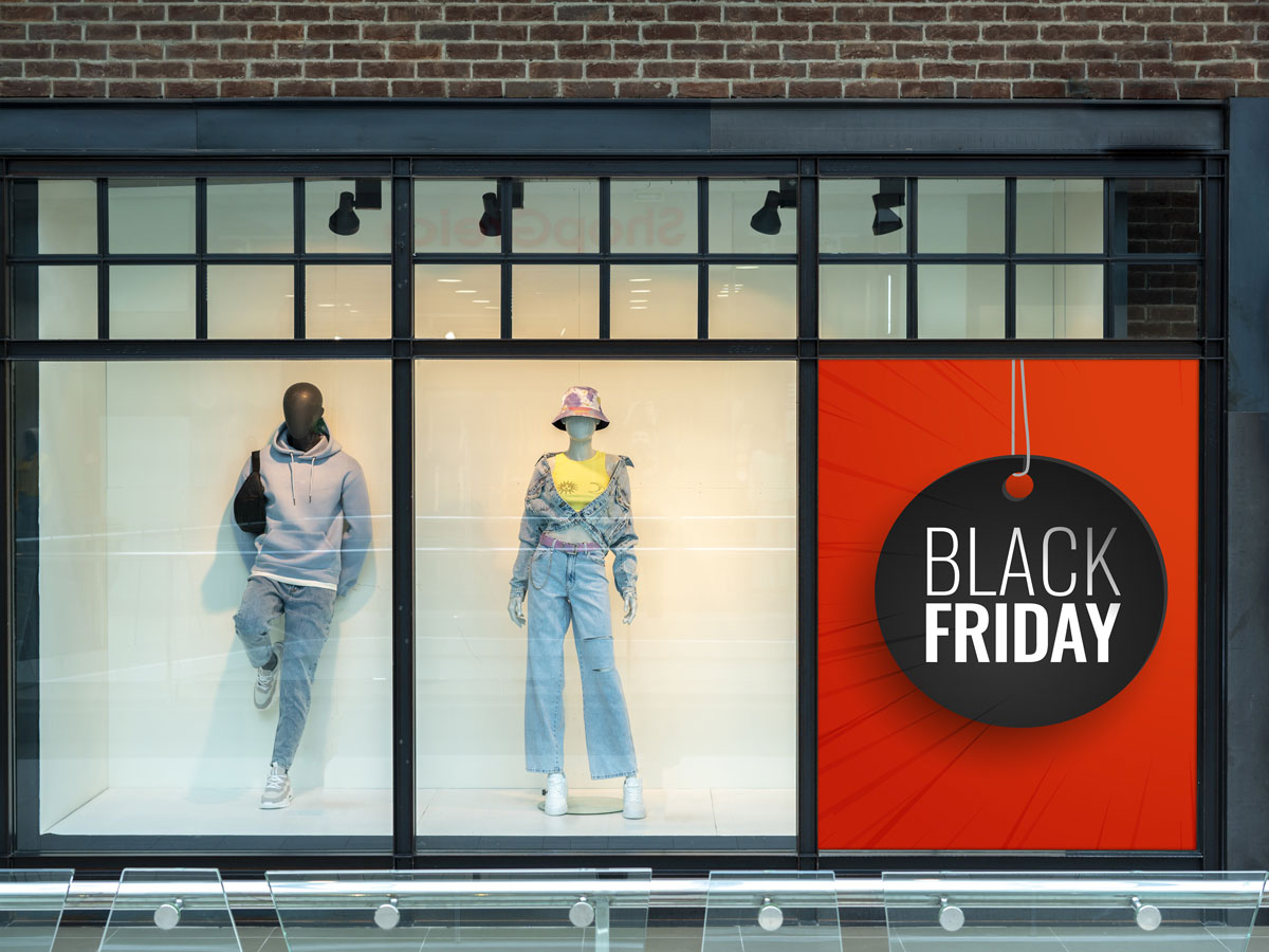 Schaufenster eines Modegeschäfts mit roter Black-Friday-Aktionsfläche neben sichtbaren Schaufensterpuppen.
