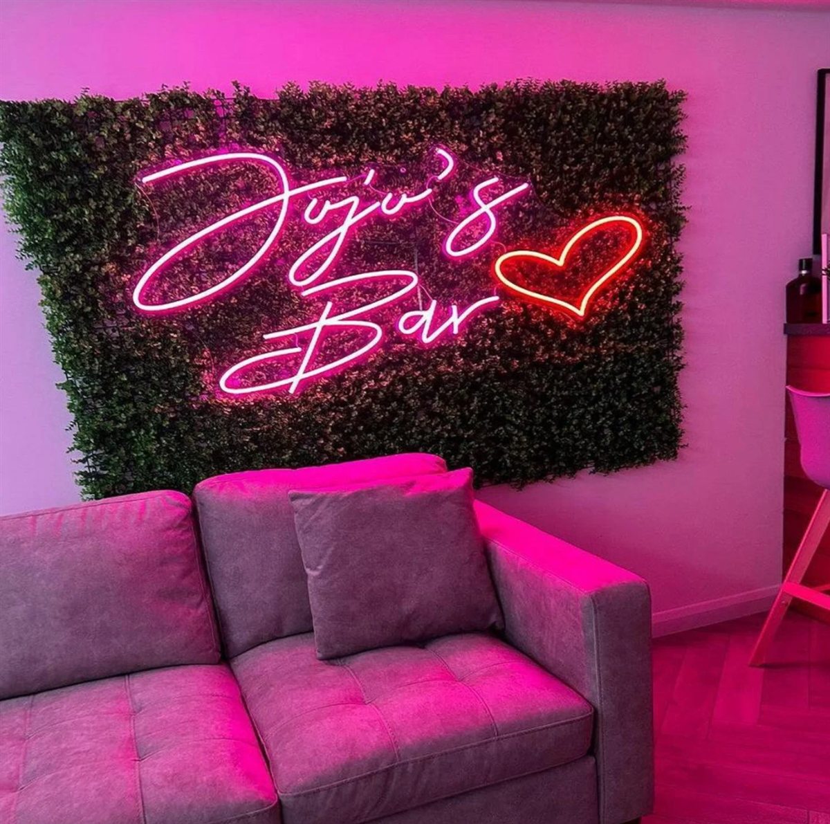 Pinker Neon-Schriftzug Jojos Bar auf einer begrünten Wand über einer Sitzlandschaft