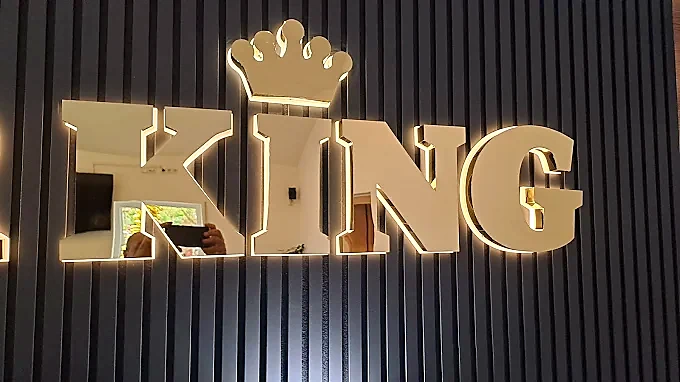 Beleuchtete KING 3D-Buchstaben auf einer dunklen Lamellenwand.