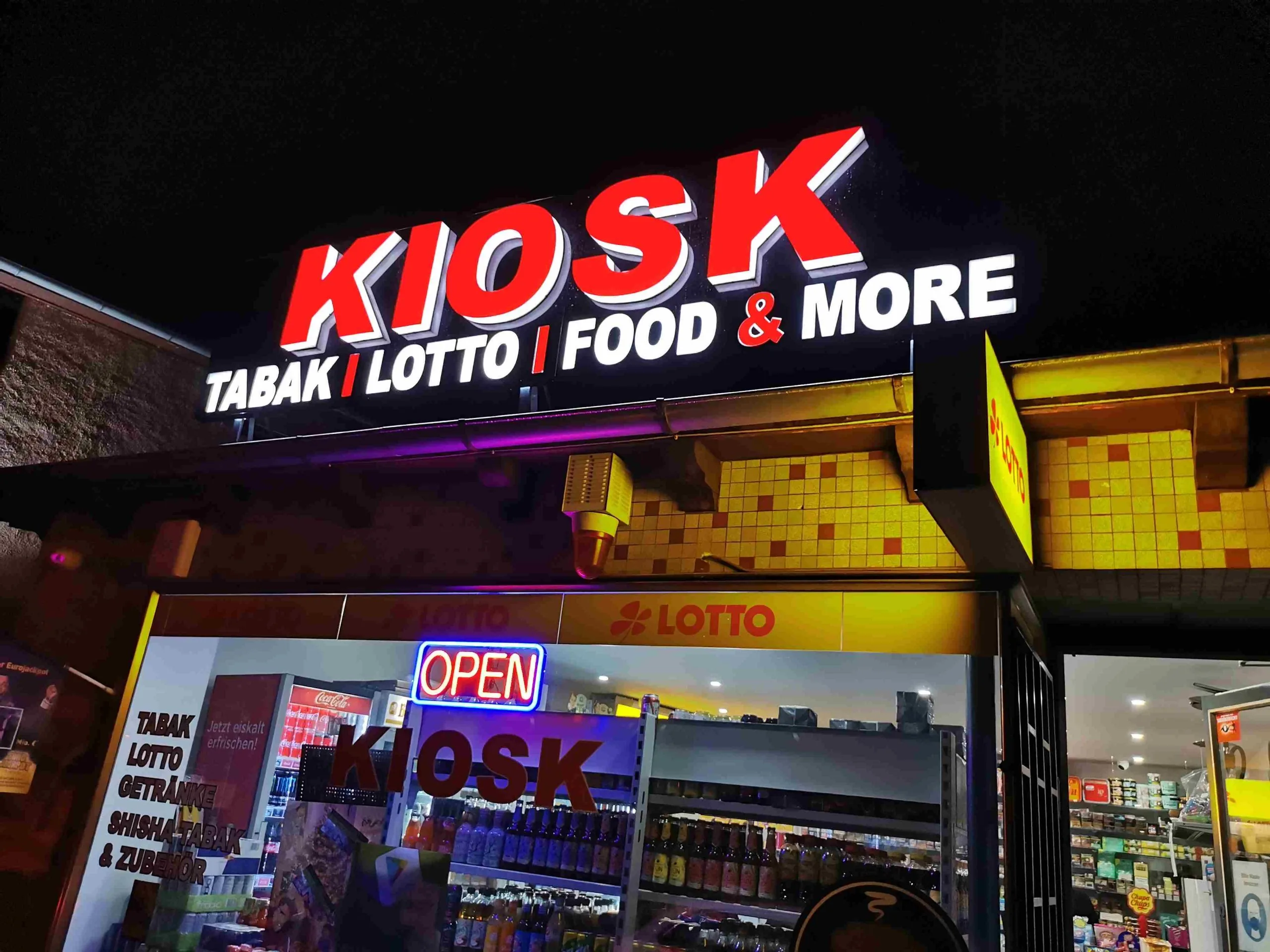 Beleuchtete rote und weiße KIOSK Profilbuchstaben an einer Ladenfassade bei Nacht